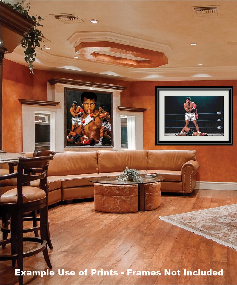 May include: A living room interior with a brown leather sectional sofa, a glass-top coffee table, and two framed boxing prints featuring Muhammad Ali. The prints are hung on a wall painted a warm orange color. The room has hardwood floors and a rug with a floral pattern.