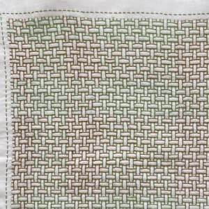 Op de afbeelding: Vierkante witte stof met een geweven patroon in groen- en bruintinten, gestikt met groen garen. De randen zijn afgewerkt met een groene stiksteek, wat een textuur en handgemaakt uiterlijk creëert.