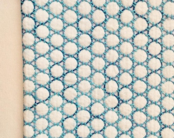 May include: Close-up of a white fabric with a repeating pattern of white circles connected by turquoise stitching. The stitching creates a geometric design. The edge of the fabric has a turquoise stitched border.