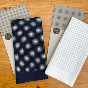 May include: Four fabric samples with grid patterns are arranged on a wooden surface. The samples feature navy blue, light blue, and grey fabrics, each with a white grid design. The text "3 mm Grid guide" is visible on the packaging.