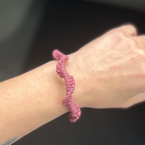 May include: A pink crocheted bracelet with a wavy design.