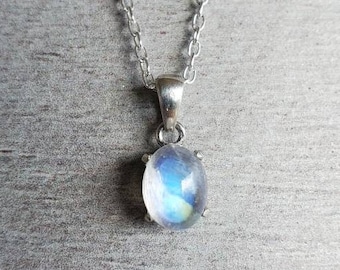 May include: A silver chain necklace with a moonstone pendant. The moonstone is oval shaped and has a light blue iridescent sheen.