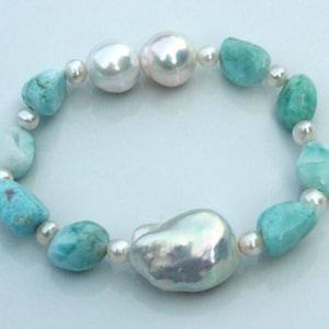 May include: A stretch bracelet featuring a series of irregular, tumbled light blue stones interspersed with small, round, white pearls. The design includes two larger, lustrous white baroque pearls and one prominent, elongated, iridescent baroque pearl.