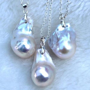 May include: Three silver necklaces with large, pearlescent, white baroque pearl pendants. The pearls are irregular in shape and have a subtle iridescent sheen.
