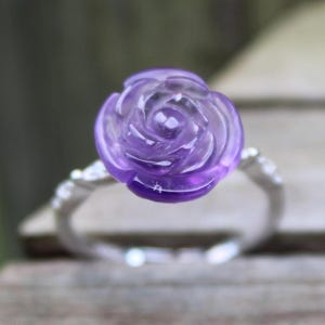 May include: A silver ring with a carved amethyst rose. The rose is a deep purple color and has a delicate design.