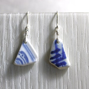 Puede incluir: Un par de pendientes hechos de fragmentos de porcelana azul y blanca con bucles de alambre plateado. Los fragmentos de porcelana son de forma irregular y tienen un patrón azul y blanco.