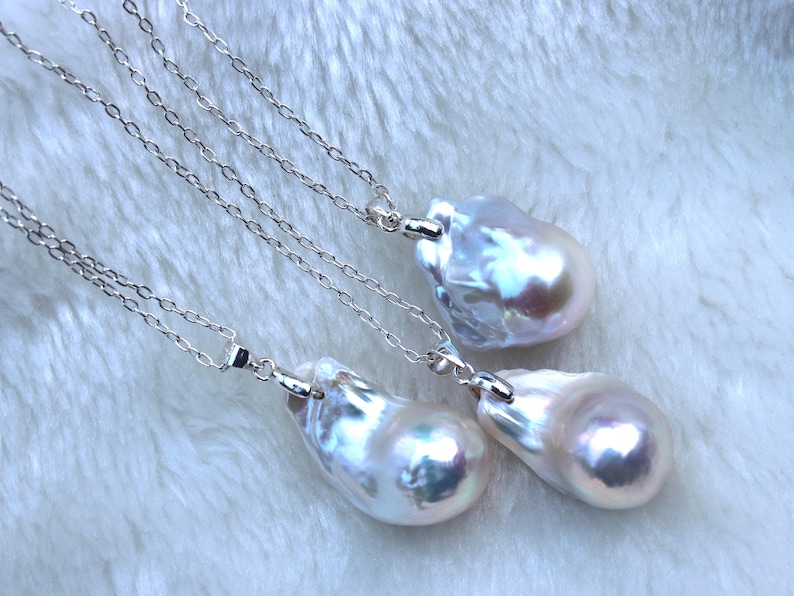 May include: Three silver chains with baroque pearl pendants. The pearls are white with iridescent hues.
