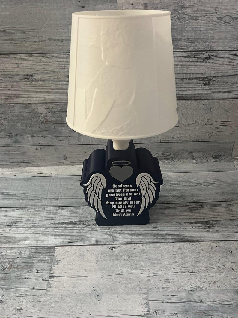 May include: A navy blue table lamp with a white lampshade. The base features a heart and wing design with the text "Goodbyes are not Forever, goodbyes are not The End they simply mean I'll Miss you Until we Meet Again."