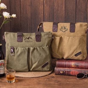 May include: Two canvas tote bags with brown leather accents and dual front pockets. The olive green bag features a mountain graphic and the text "WESTEN," while the tan bag displays the initials "EK" above a pair of stylized deer antlers.