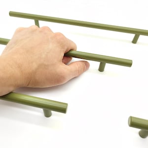 May include: A set of olive green cylindrical cabinet pulls featuring a smooth matte finish. Each pull consists of a long horizontal bar supported by two vertical posts, designed for attachment to furniture or cabinetry doors and drawers.
