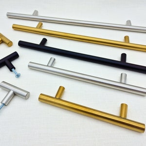 May include: A selection of cabinet handles in various finishes, including stainless steel, gold, and black. The image shows T-bar and pull handles, each with a screw for installation. Measurements are in centimetres.