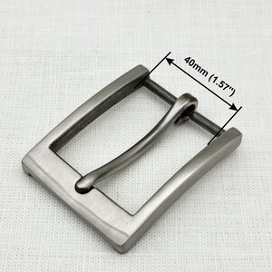 May include: A silver-toned metal belt buckle with a rectangular frame and a curved, smooth buckle tongue. The buckle measures 1.57 inches (40 mm) wide.