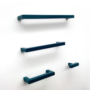 May include: A set of four dark teal cabinet hardware pieces, including three rectangular bar pulls of varying lengths and one single-post T-shaped knob, all featuring a smooth, matte finish and clean, angular lines.