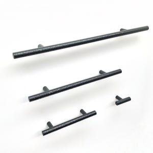Op de afbeelding: Een set van vier zwarte kastgrepen en een T-vormige knop, allemaal met een getextureerde, matte afwerking. De set bevat drie cilindrische staafgrepen van verschillende lengtes en één kleine knop, elk voorzien van twee bevestigingspunten.