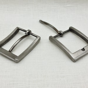 May include: Two silver metal belt buckles. One buckle is closed and the other is open. The buckles are both rectangular with rounded corners.