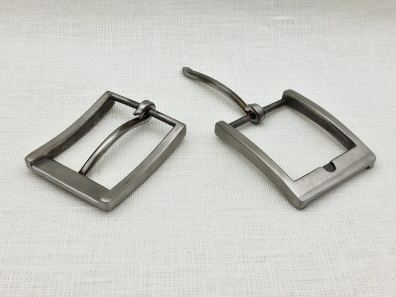May include: Two silver metal belt buckles. One buckle is closed and the other is open. The buckles are both rectangular with rounded corners.