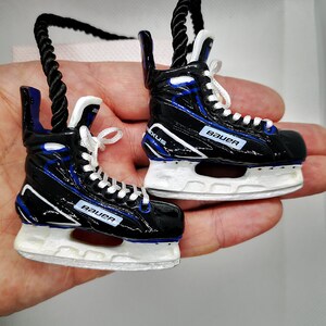 May include: A pair of black and blue hockey skate ornaments with white blades and the word "Bauer" printed on each skate.