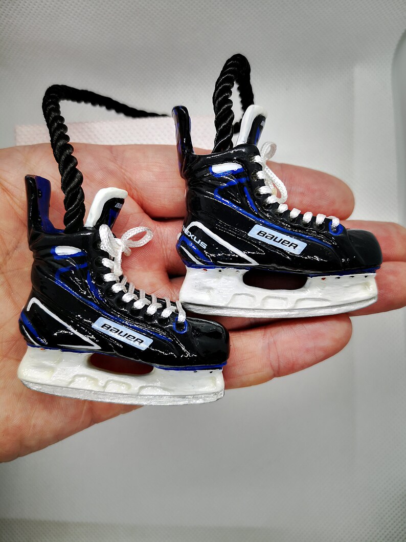 May include: A pair of black and blue hockey skate ornaments with white blades and the word "Bauer" printed on each skate.