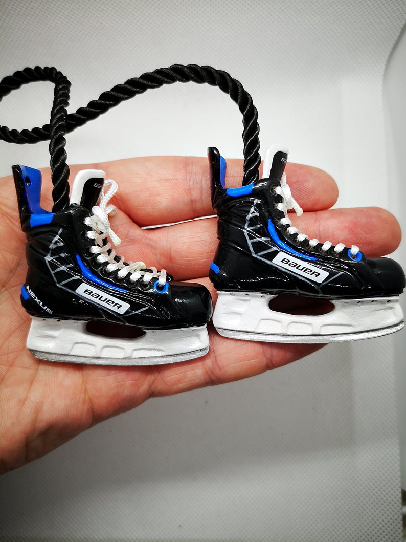 May include: A pair of black and blue ice hockey skates with white blades. The skates have the word "Bauer" printed on the side. The skates are attached to a black rope.