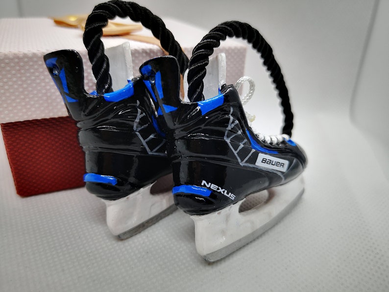 May include: A pair of black and blue hockey skate ornaments with white blades. The skates are decorated with a white and gray pattern and the words "Bauer" and "Nexus".