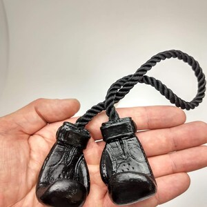 Puede incluir: Un par de llaveros de guantes de boxeo negros unidos a una cuerda trenzada negra.