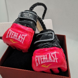May include: A pair of pink and black boxing gloves with the word "EVERLAST" printed on each glove. The gloves are tied together with a black rope.