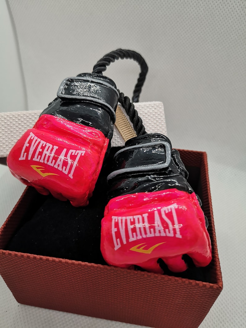 May include: A pair of pink and black boxing gloves with the word "EVERLAST" printed on each glove. The gloves are tied together with a black rope.