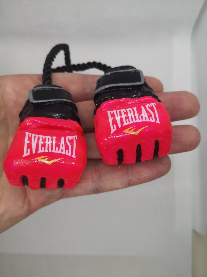 May include: A pair of pink boxing gloves with black trim and the word "EVERLAST" in white lettering with a gold logo. The gloves are connected by a black rope.