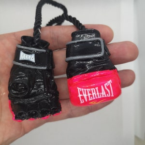May include: A pair of black boxing gloves with pink trim. One glove has the word "MMA" on the wrist strap and the other has the word "EVERLAST" on the pink trim.