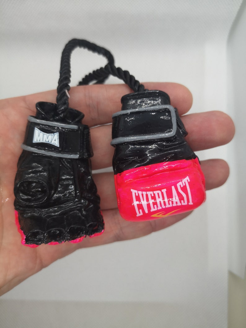 May include: A pair of black boxing gloves with pink trim. One glove has the word "MMA" on the wrist strap and the other has the word "EVERLAST" on the pink trim.