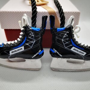 May include: A pair of black and blue hockey skate ornaments with white laces and the words "Bauer" and "Nexus" on them.