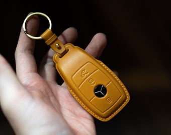 May include: A tan leather key fob with a silver Mercedes-Benz logo and buttons.