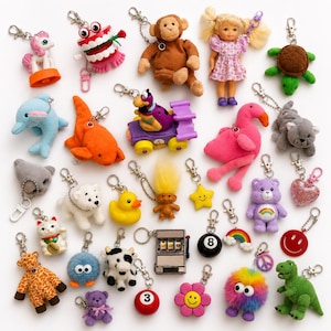 May include: A collection of various plush and plastic keychains featuring diverse characters including a monkey, a doll, a turtle, a dolphin, a flamingo, a Care Bear, a slot machine, a rubber duck, a troll, and several animal figures.