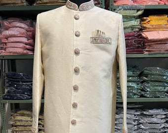 Könnte beinhalten: Eine cremefarbene, langärmelige Kurta mit einem Mandarinkragen und einer dekorativen Tasche auf der linken Seite. Die Kurta ist mit einem floralen Muster am Kragen und an der Tasche bestickt und hat eine Reihe von perlmuttartigen Knöpfen an der Vorderseite.