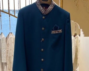 May include: A teal blue men's kurta with a gold button closure and a decorative embroidered collar. The kurta is hanging on a gold stand in a retail store.