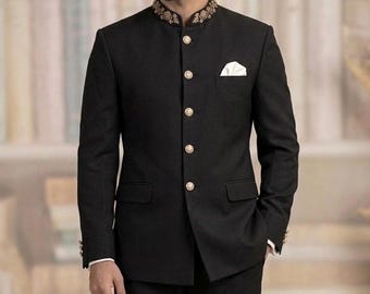 Puede incluir: Un traje bandhgala negro con cuello alto con intrincados bordados dorados, cinco botones dorados redondos en la parte delantera y un pañuelo de bolsillo blanco. El conjunto incluye pantalones negros a juego y zapatos de vestir de cuero negro.