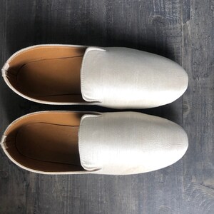 Peut inclure: Une paire de chaussures blanches en satin &agrave; enfiler avec une semelle int&eacute;rieure en cuir marron.