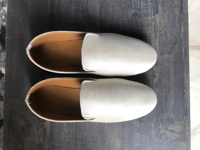 Peut inclure: Une paire de chaussures blanches en satin &agrave; enfiler avec une semelle int&eacute;rieure en cuir marron.