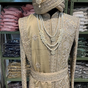 May include: A gold embroidered men's outfit with a matching turban. The outfit features intricate silver embroidery and a pearl necklace.