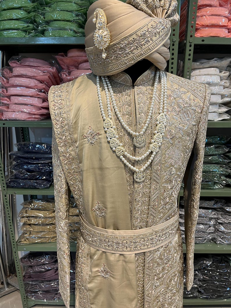 May include: A gold embroidered men's outfit with a matching turban. The outfit features intricate silver embroidery and a pearl necklace.
