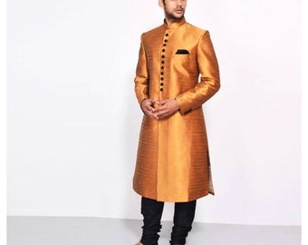 May include: A long, gold-coloured, button-up jacket with a mandarin collar. The jacket has a black trim around the collar and buttons. The person wearing the jacket is standing with their hands clasped in front of them.