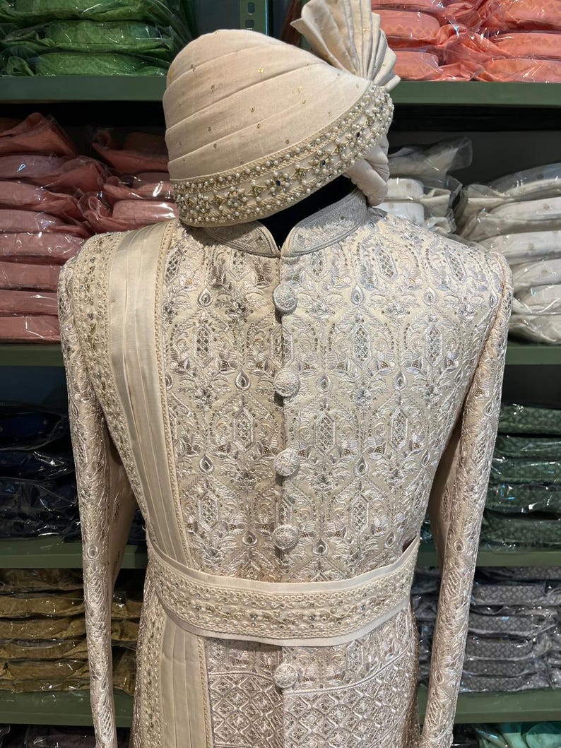 Puede incluir: Un sherwani blanco para hombre bordado con un turbante blanco a juego. El sherwani tiene un dise&ntilde;o de hilo plateado y una faja blanca. El turbante tiene un adorno de perlas.