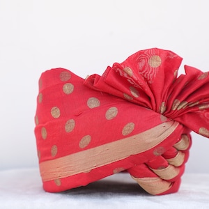 May include: A red turban with gold polka dots and a gold trim. The turban is folded into a decorative shape.