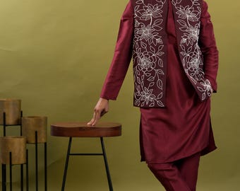 May include: Burgundy kurta pajama set with a matching vest featuring white floral embroidery. The outfit includes a long-sleeved tunic top and straight-leg pants. The model is wearing brown embellished shoes.