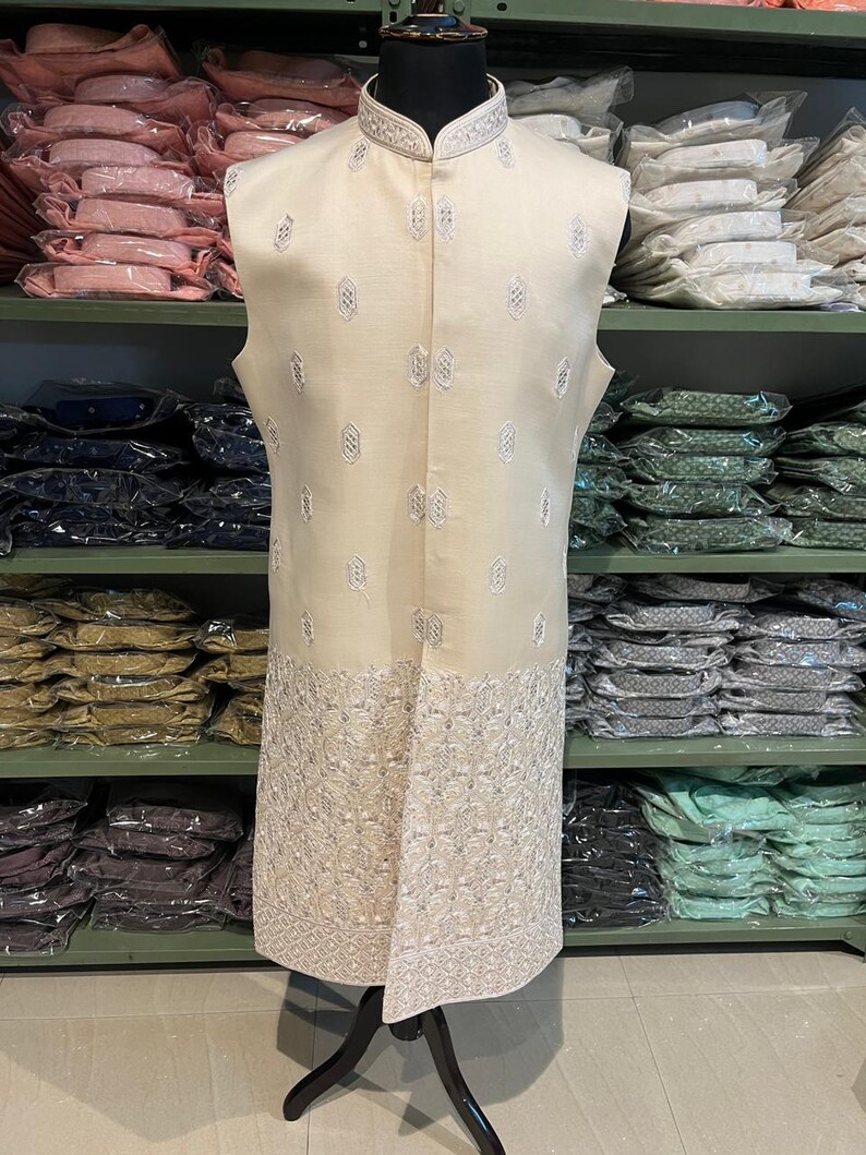 Puede incluir: Un chaleco sin mangas de color crema con bordados plateados. El chaleco tiene un cuello mandar&iacute;n y cierre de bot&oacute;n. El bordado es intrincado y presenta un dise&ntilde;o floral.