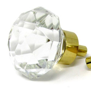 May include: Two clear glass door knobs with gold metal bases. The knobs are faceted and have a diamond-like shape.