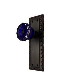 May include: A black door knob with a cobalt blue glass knob. The door knob has a decorative border around the plate.