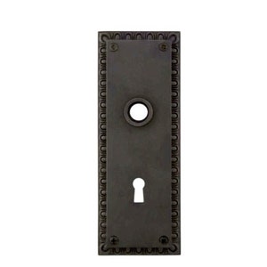 May include: A black metal door plate with a keyhole and a decorative border. The plate is rectangular and has a slightly aged finish.
