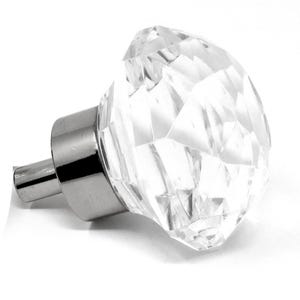 May include: A clear, faceted crystal cabinet knob with a silver-toned base and stem. The knob's design resembles a large gemstone, reflecting light. This decorative hardware is suitable for drawers and cabinets.