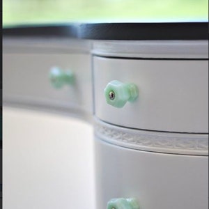 May include: White vanity with two drawers and green glass knobs. The vanity has a decorative trim around the drawers.